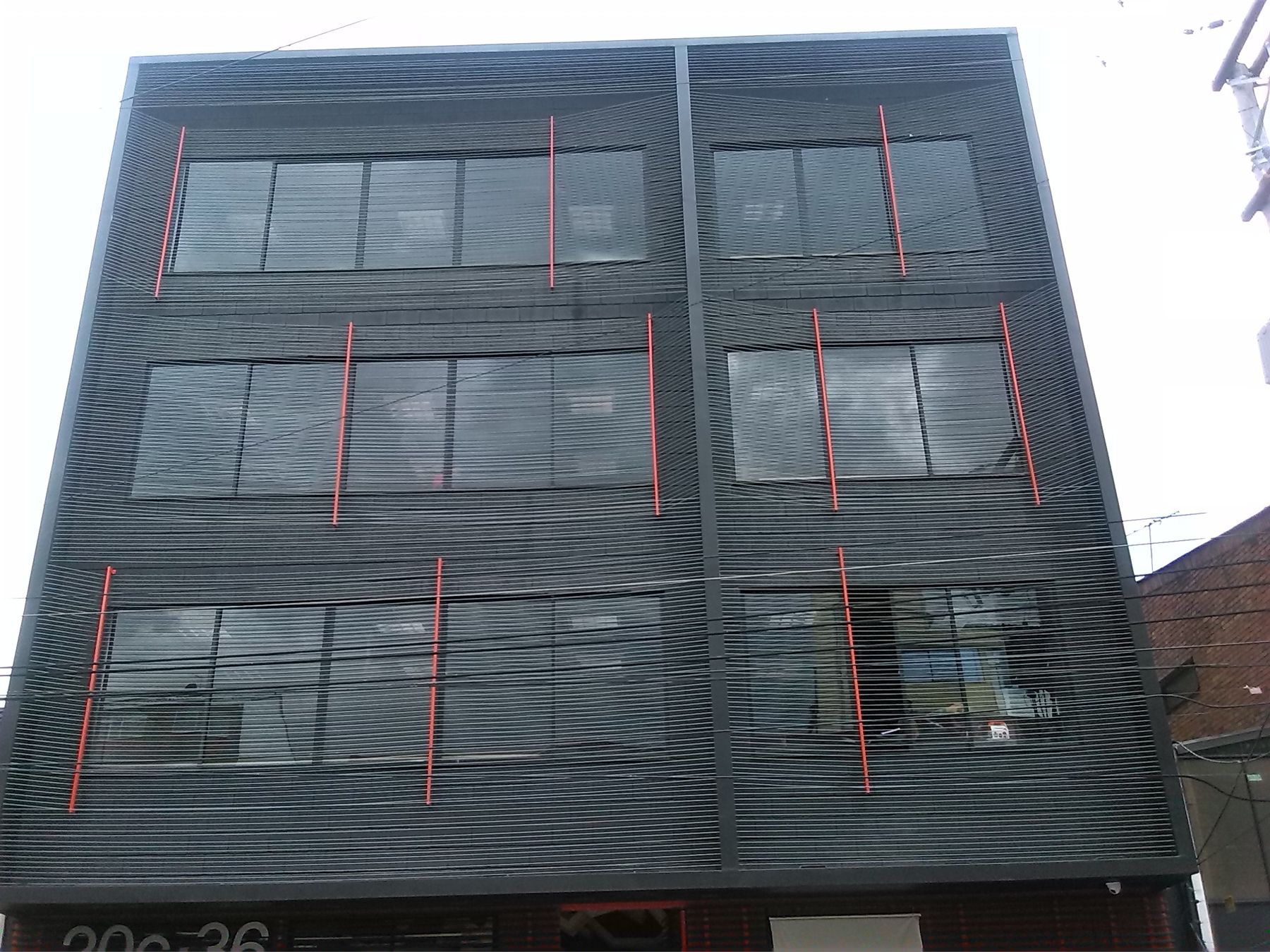 Fachada sobre la Calle 75A, con celosía oscura y montantes naranja